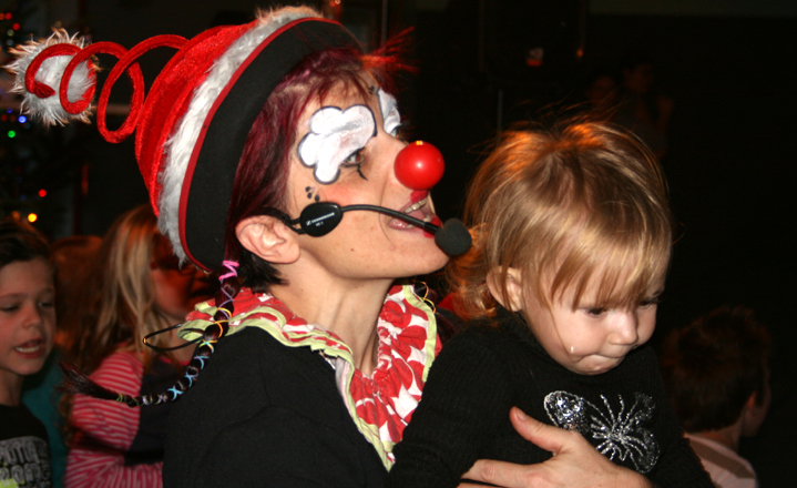Photo d'Anita le clown sur scène avec chapeau de Noël et fillette dans les bras