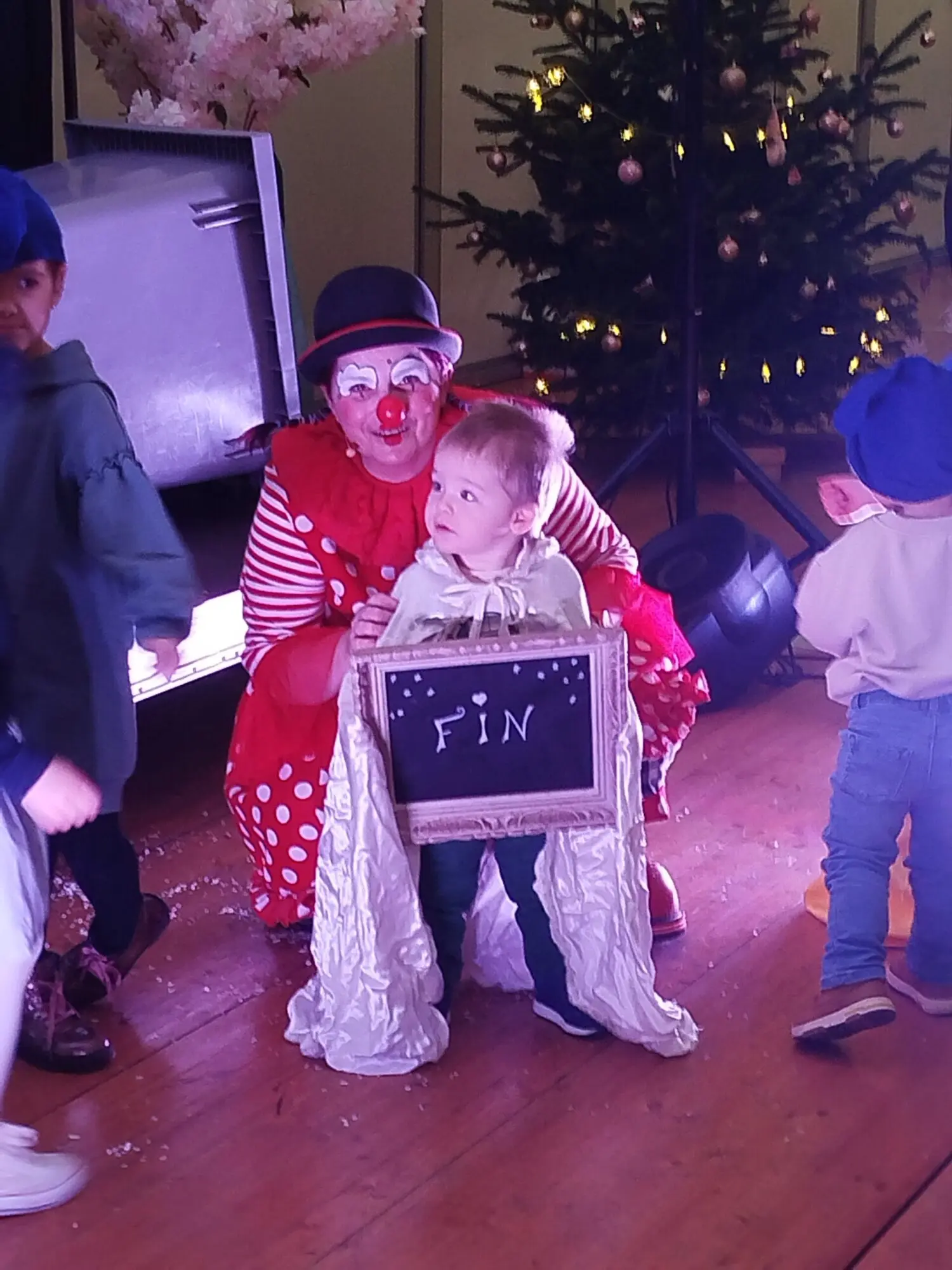 Photo d'Anita le clown sur scène avec petit garçon portant le panneau "Fin"